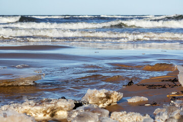 
a wavy sea and a sandy beach partially covered with ice chunks.