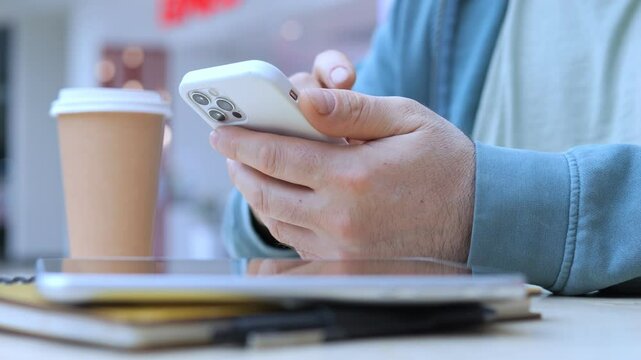 Man is sitting at a table with a white iPhone in his hand and a cup of coffee in front of him