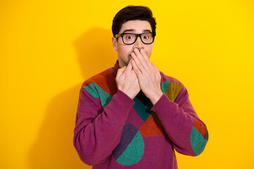 Expressive young man surprised with a covering hands gesture on a vibrant yellow background in...