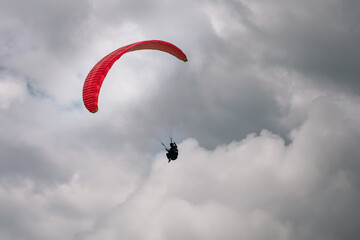 Paragliding flight in dramatic cloudy sky. Hang gliders silhouette with parachute against white clouds