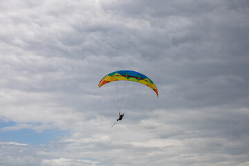 Paragliding flight in dramatic cloudy sky. Hang gliders silhouette with parachute against white clouds