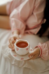 A wooden tray with a polaroid photo and a cup of tea on a white bedspread. The photo features a close-up of a person's face, while the cup has a decorative design.