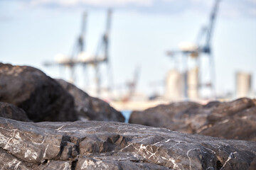 Rocks in foreground with blurred industrial cranes in background