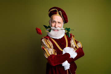 Elderly man in ornate medieval costume holding a rose with fun and elegant expression, on khaki...