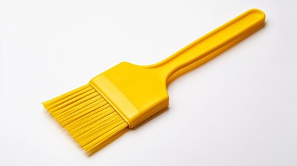 A yellow basting brush with a plastic handle and bristles on a white surface in a studio shot