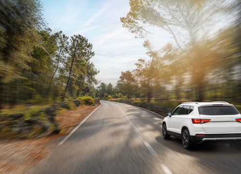 A white SUV drives swiftly down a sunlit forest road, capturing the spirit of freedom, speed, and outdoor adventure.