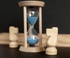 Hourglass with a flowing blue sand inside and wooden chess knights	