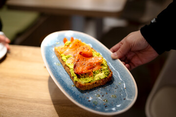 Waiter serving avocado toast with smoked salmon and spices in restaurant