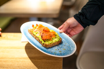 Waiter serving smoked salmon and avocado toast in restaurant