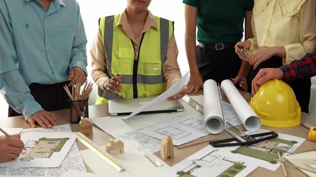 Smart architect and safety engineer discussion about building blueprint on table with architectural document, measurement tools and wooden block scatter around at modern office. Closeup. Delineation.