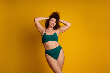 Obraz premium Confident young woman in green lingerie posing naturally against a bright yellow background, promoting self acceptance, body positivity