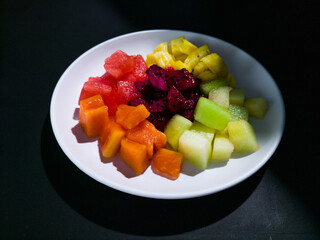 a round white plate with fruits salad on black background