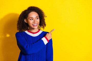 Smiling young woman in vibrant sweater posing against bright yellow background, showing gesture...
