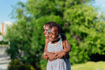 Two young african american twin sisters are hugging each other in a park during summer