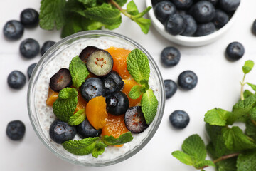 Delicious chia pudding with blueberries, peaches and mint in glass on white table, flat lay