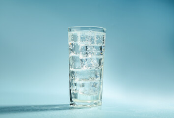 Soda water with ice cubes in glass on light blue background
