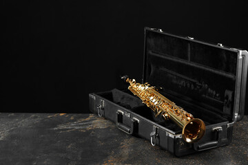 Jazz. Golden saxophone in case on black textured table, space for text