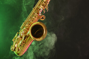 Fototapeta premium Golden saxophone on dark background with green light and smoke, closeup. Space for text