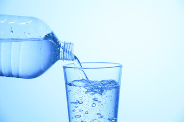 Pouring soda water from bottle into glass on light blue background, closeup. Space for text
