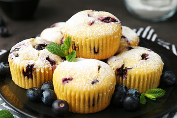 Delicious muffins with blueberries, powdered sugar and mint on dark table, closeup