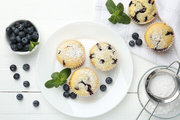 Delicious muffins with blueberries, powdered sugar and mint on white wooden table, flat lay