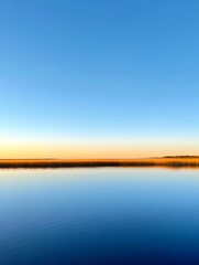 Fototapeta premium Serene Sunset Over Calm Water - Peaceful sunset scene featuring a calm body of water reflecting the sky and a distant shoreline. Tranquil and serene