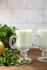 Healthy parsley drink in glasses and leaves on wooden table, closeup