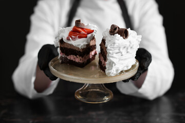 Confectioner with pieces of tasty cake at black marble table in kitchen, closeup