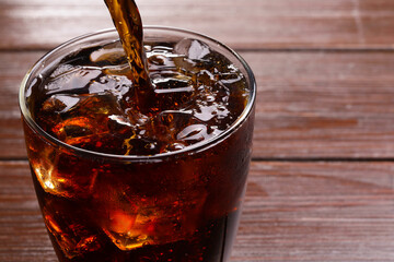 Pouring refreshing cola into glass at wooden table, closeup. Space for text