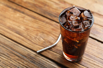 Refreshing cola with ice cubes in glass on wooden table, closeup. Space for text