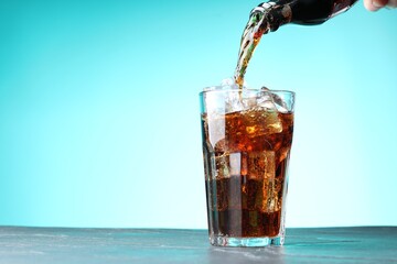 Pouring refreshing cola into glass at dark table against turquoise gradient background. Space for...