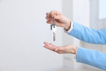 Real estate agent holding key with house shaped keychain indoors, closeup. Space for text