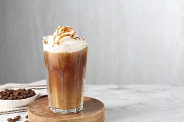 Tasty iced coffee with whipped cream, syrup and beans on white marble table. Space for text