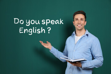 Teacher pointing at green chalkboard with phrase Do You Speak English?