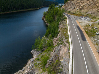 Aerial view of curved road alongside lush green forest and tranquil lake waters