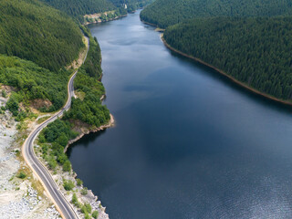 Aerial view of curved road alongside lush green forest and tranquil lake waters