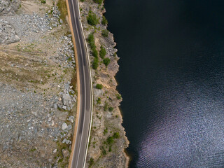 Aerial view of curved road alongside lush green forest and tranquil lake waters