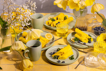 Yellow lemon pancakes with blueberries and mint on a table decorated with yellow tulips