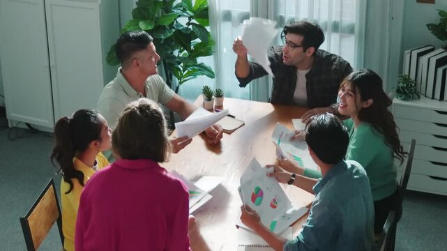 Top view of smart people throw paper and giving high five at meeting table with financial document and stock market analysis paper scattering around. Aerial view of team celebrate project. Symposium.