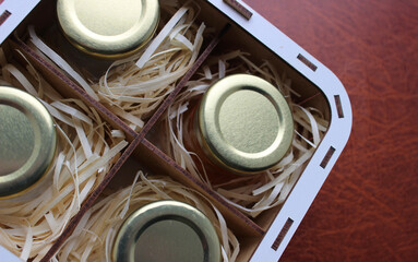 Gift Set of Craft Honey in Small Jars in Wooden Box with Shavings. Craft Beekeeping Products on Brown Leather Surface
