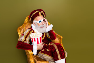 Elderly nobleman in renaissance costume with 3D glasses and popcorn on vintage throne chair against...