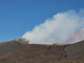 Active volcanic crater on Mount Etna releasing thick white smoke, surrounded by dark lava rocks and...