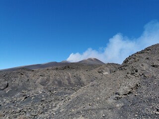 Rocky volcanic terrain with scattered lava stones and slopes surrounding a smoking crater on Mount...