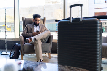 A stylish businessman is sitting comfortably in a modern lounge area, deeply engrossed in his phone...