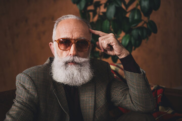 Elegant senior man with a stylish beard wearing a retro plaid suit seated indoors with nostalgic decor