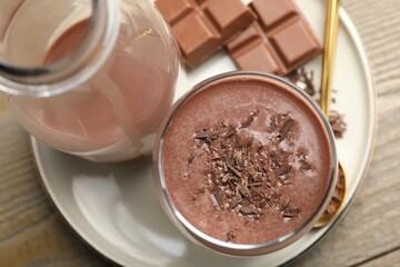 Tasty chocolate milk with shavings and pieces on wooden table, top view