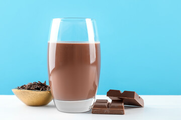 Tasty chocolate milk with shavings and pieces on white table against light blue background
