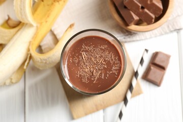 Tasty chocolate milk in glass, banana and pieces on white wooden table, flat lay