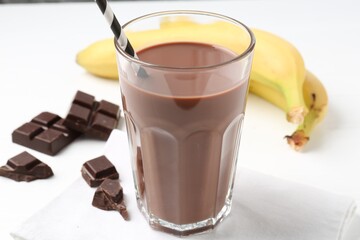Tasty chocolate milk in glass, pieces and bananas on white table, closeup