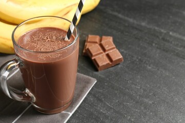 Tasty chocolate milk in glass cup, pieces and bananas on black table, closeup. Space for text